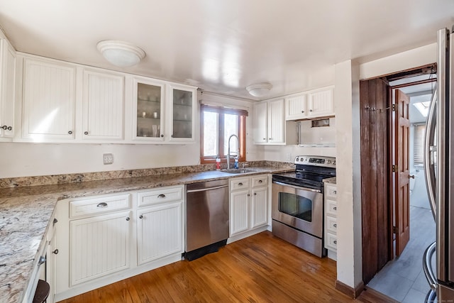 kitchen featuring white cabinets, glass insert cabinets, wood finished floors, stainless steel appliances, and a sink