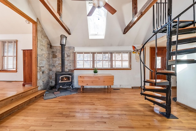 unfurnished room featuring ceiling fan, stairway, wood finished floors, a wood stove, and high vaulted ceiling