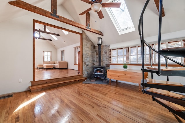 unfurnished living room featuring a wood stove, a skylight, hardwood / wood-style floors, and beamed ceiling