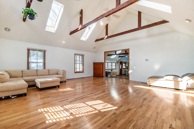 living room with high vaulted ceiling, beamed ceiling, a skylight, and light wood-style floors