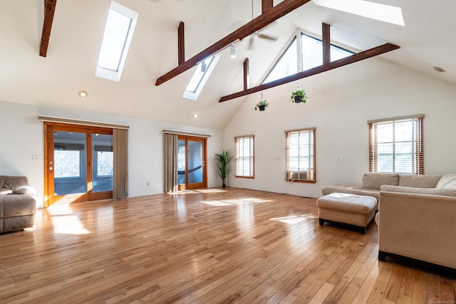 living area featuring a skylight, high vaulted ceiling, light wood finished floors, and beam ceiling