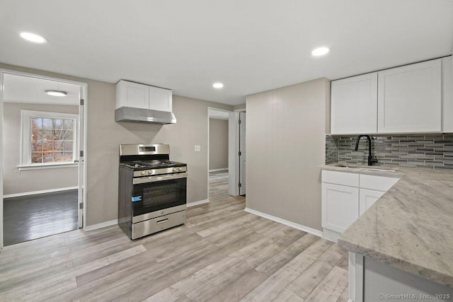 kitchen featuring stainless steel gas range oven, light stone counters, under cabinet range hood, a sink, and light wood-type flooring