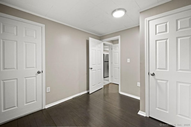 unfurnished bedroom with dark wood-style floors, freestanding refrigerator, ornamental molding, and baseboards