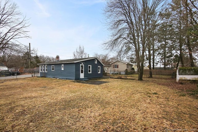 back of property with a chimney, fence, and a lawn