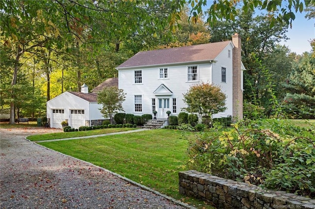 colonial-style house with gravel driveway, a front lawn, a chimney, an outbuilding, and an attached garage