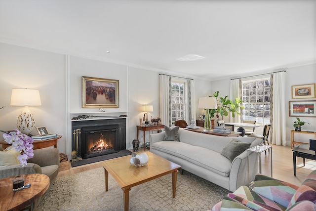 living area featuring a warm lit fireplace, light wood finished floors, and ornamental molding