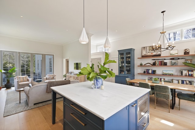 kitchen featuring stainless steel microwave, crown molding, light wood-type flooring, a notable chandelier, and blue cabinets