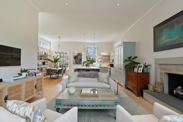 living area with a premium fireplace, a notable chandelier, ornamental molding, and light wood finished floors