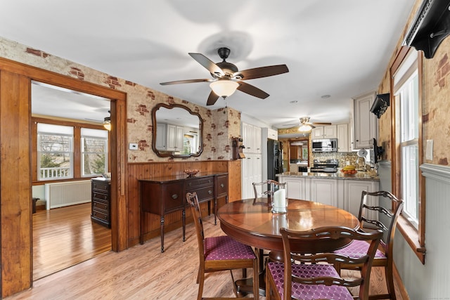 dining room featuring a ceiling fan, wainscoting, light wood-style flooring, and radiator