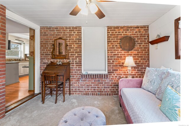 living area featuring carpet, ceiling fan, and brick wall