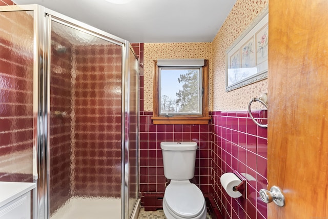 full bathroom with wallpapered walls, a stall shower, toilet, a wainscoted wall, and tile walls