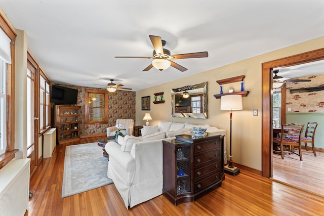 living room with wallpapered walls, radiator heating unit, wood finished floors, and a healthy amount of sunlight