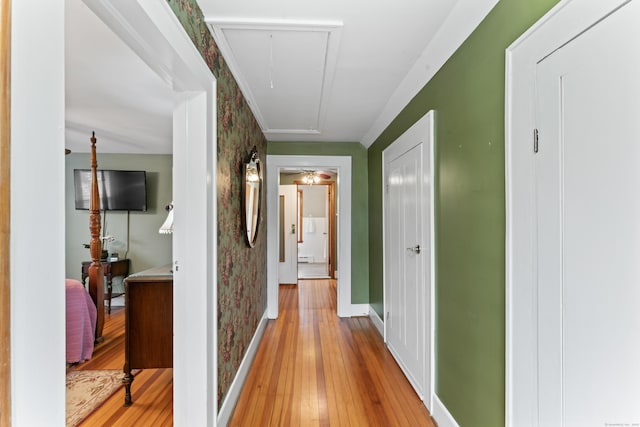 corridor with attic access, light wood-style flooring, and baseboards