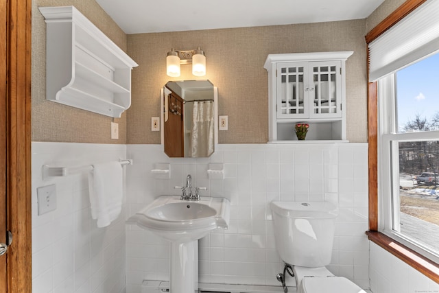 full bath featuring a wainscoted wall, tile walls, toilet, and wallpapered walls