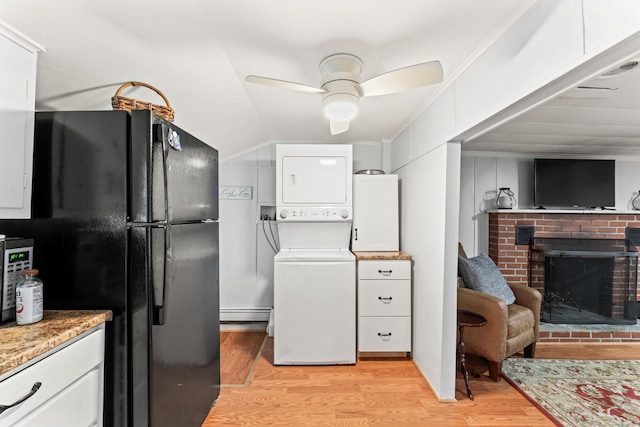 kitchen with a brick fireplace, white cabinets, light wood-style floors, freestanding refrigerator, and stacked washing maching and dryer