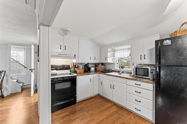 kitchen featuring light wood finished floors, white cabinetry, a sink, under cabinet range hood, and black appliances