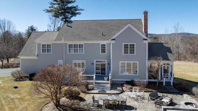 back of property with a wooden deck, a shingled roof, a chimney, and a patio area