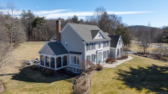 rear view of house with a lawn, a chimney, and a sunroom