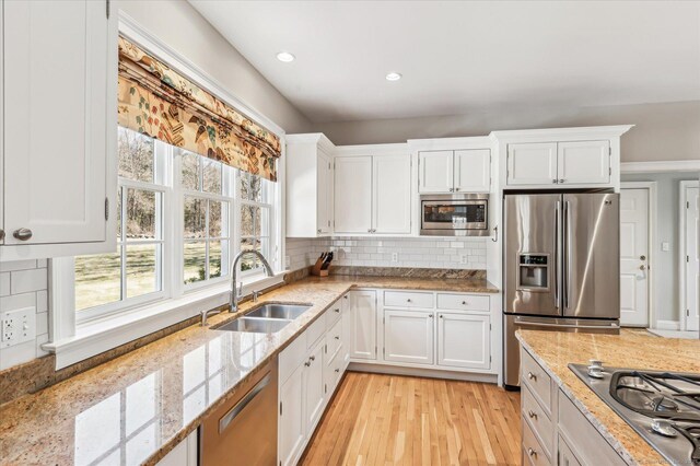 kitchen featuring a sink, white cabinetry, appliances with stainless steel finishes, decorative backsplash, and light stone countertops