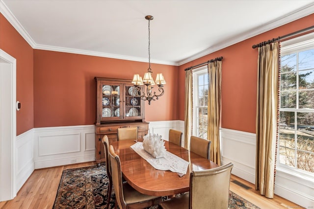 dining space featuring visible vents, crown molding, a chandelier, a wainscoted wall, and light wood-type flooring