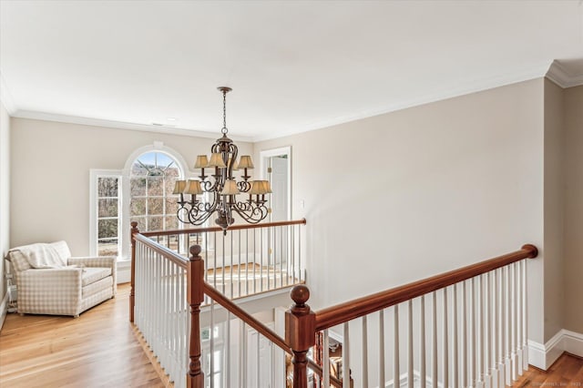 hallway with baseboards, light wood-style floors, crown molding, an upstairs landing, and a chandelier