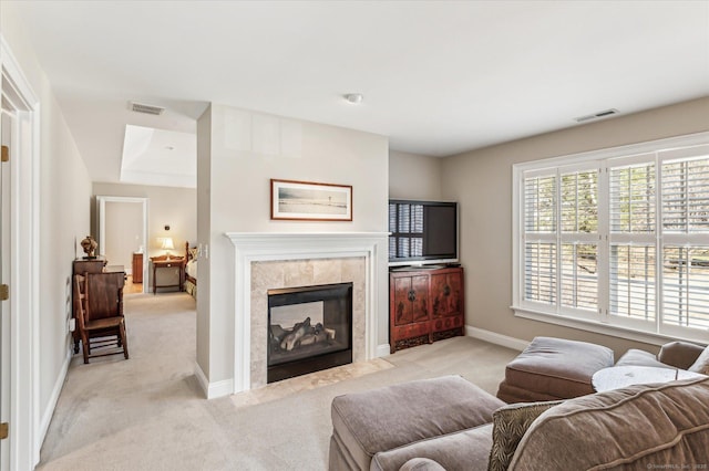 living area featuring a tiled fireplace, visible vents, light colored carpet, and baseboards