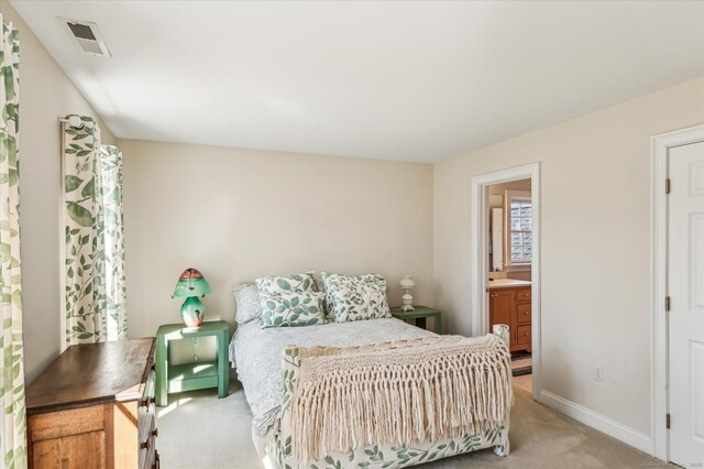 bedroom featuring visible vents, baseboards, light colored carpet, and ensuite bathroom