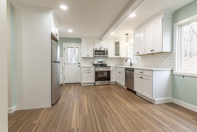 kitchen with wood finished floors, light countertops, white cabinets, appliances with stainless steel finishes, and tasteful backsplash