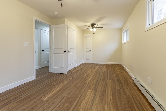 unfurnished bedroom with multiple windows, wood finished floors, baseboards, and baseboard heating