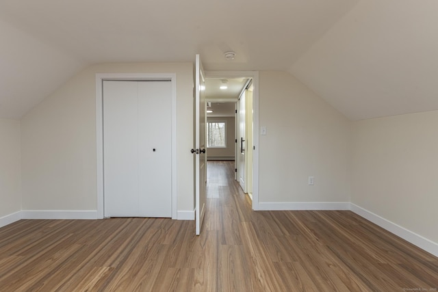 additional living space featuring a baseboard radiator, baseboards, wood finished floors, and vaulted ceiling