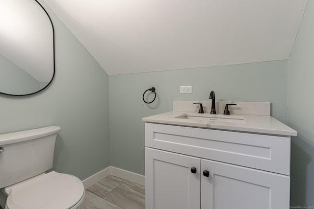 bathroom featuring baseboards, lofted ceiling, toilet, and vanity