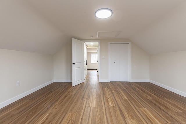 additional living space with baseboards, attic access, wood finished floors, and vaulted ceiling