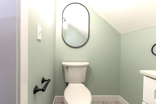 half bathroom featuring toilet, vanity, baseboards, and wood finished floors