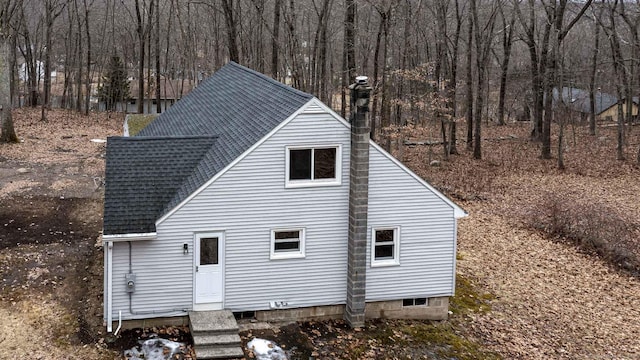 back of house with roof with shingles and a wooded view