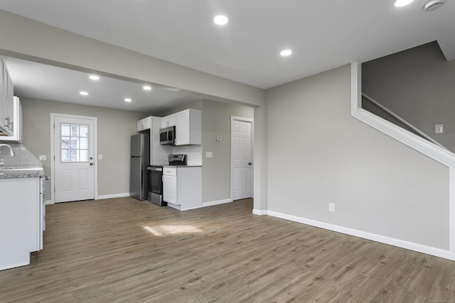 kitchen with stainless steel appliances, wood finished floors, baseboards, white cabinets, and backsplash