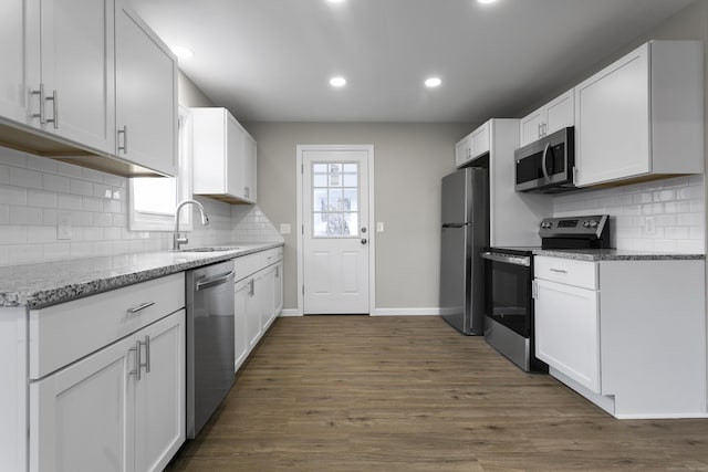 kitchen featuring dark wood-style floors, appliances with stainless steel finishes, white cabinetry, a sink, and light stone countertops