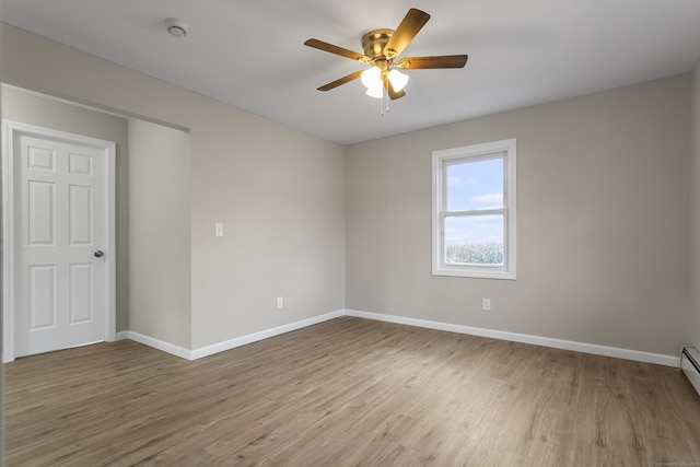 spare room with baseboard heating, wood finished floors, a ceiling fan, and baseboards