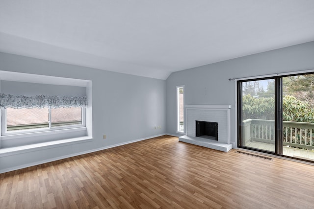 unfurnished living room with a brick fireplace, visible vents, vaulted ceiling, and wood finished floors