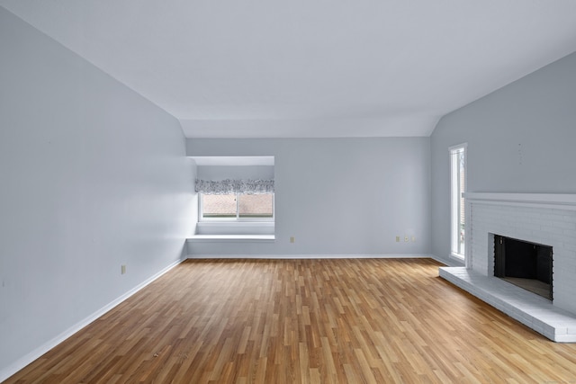 unfurnished living room featuring a brick fireplace, baseboards, vaulted ceiling, and wood finished floors