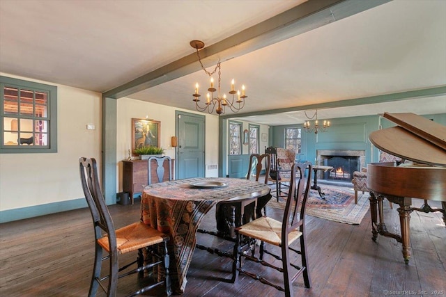 dining area featuring beam ceiling, a warm lit fireplace, baseboards, a chandelier, and dark wood-style flooring