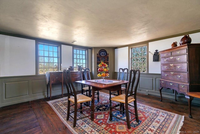 dining area featuring a wainscoted wall, dark wood finished floors, and a decorative wall