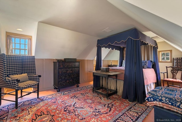 bedroom featuring visible vents, wood walls, wainscoting, and vaulted ceiling