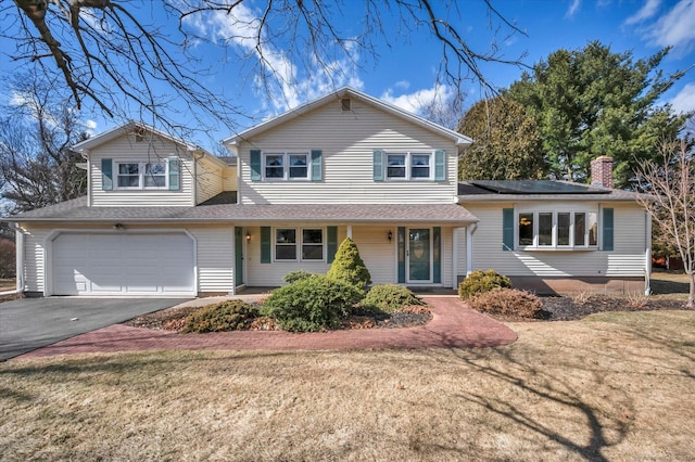 split level home featuring driveway, a garage, a shingled roof, roof mounted solar panels, and a front yard