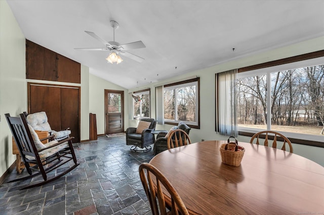 dining space with lofted ceiling, a ceiling fan, stone tile flooring, and baseboards