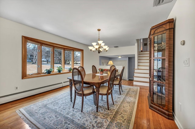 dining space featuring a notable chandelier, a baseboard radiator, visible vents, wood finished floors, and stairs