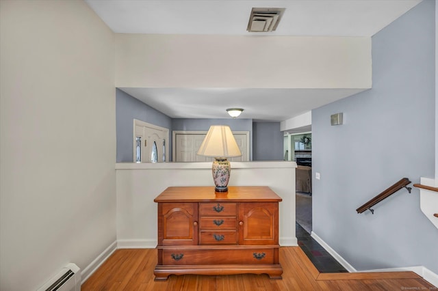 interior space featuring baseboards, visible vents, a baseboard radiator, wood finished floors, and an upstairs landing