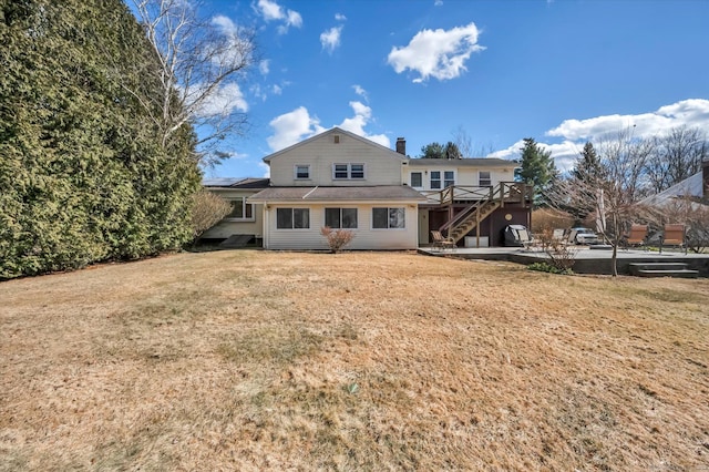 back of house featuring a deck, a chimney, a lawn, and stairway