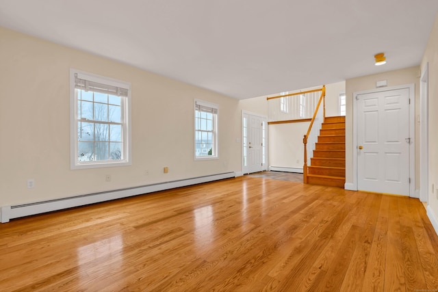 unfurnished living room with a baseboard heating unit, light wood-style flooring, and stairs