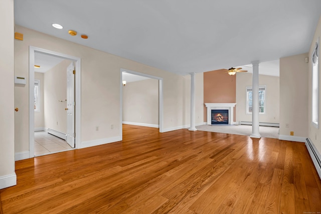 unfurnished living room featuring a glass covered fireplace, decorative columns, light wood-type flooring, and a baseboard heating unit