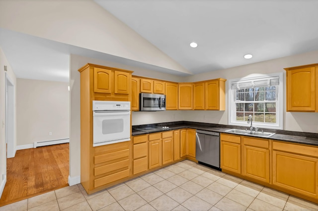 kitchen featuring dark countertops, vaulted ceiling, baseboard heating, stainless steel appliances, and a sink